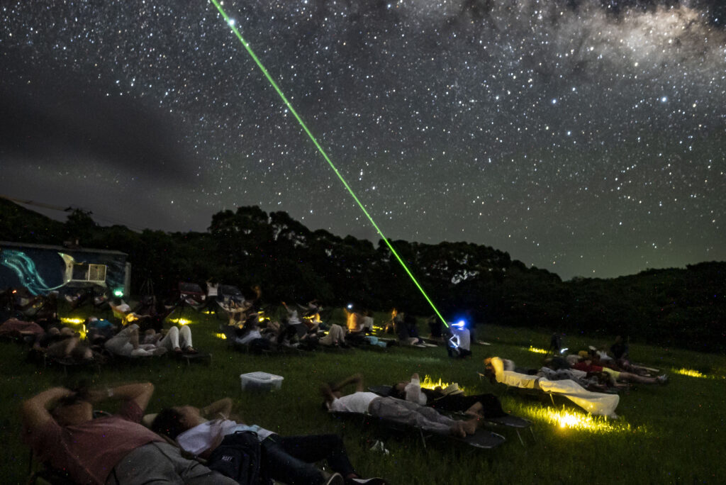 Tour guide using laser pointer for star guide while guests relax on recliners at Nagareboshi no Oka, Ishigaki Island