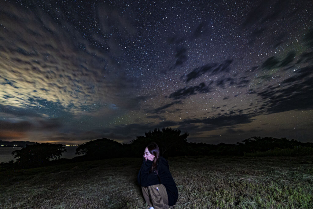 Woman sitting in grass field gazing at the starry sky at Nagareboshi no Oka, Ishigaki Island