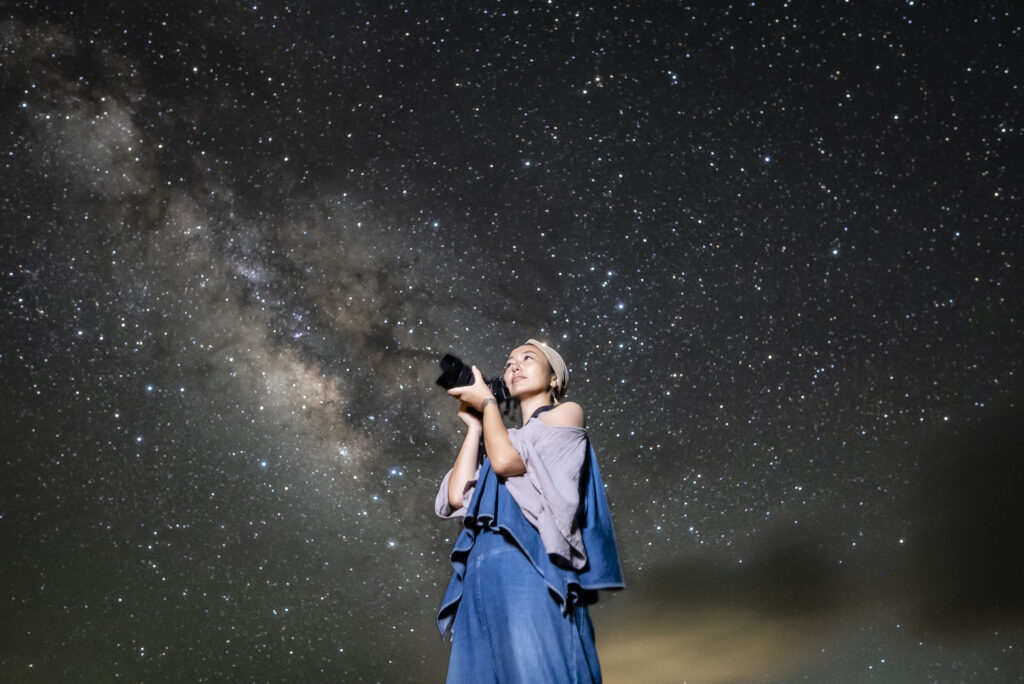 Woman photographer holding camera under the Milky Way at Nagareboshi no Oka stargazing spot, Ishigaki Island