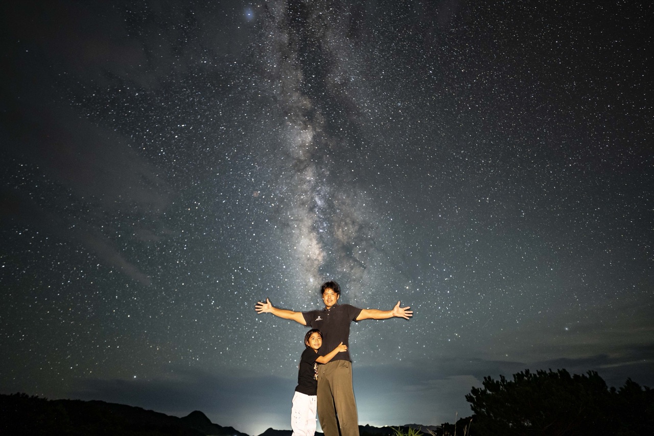 Father child arms wide open milky way at Nagareboshi no Oka stargazing spot, Ishigaki Island